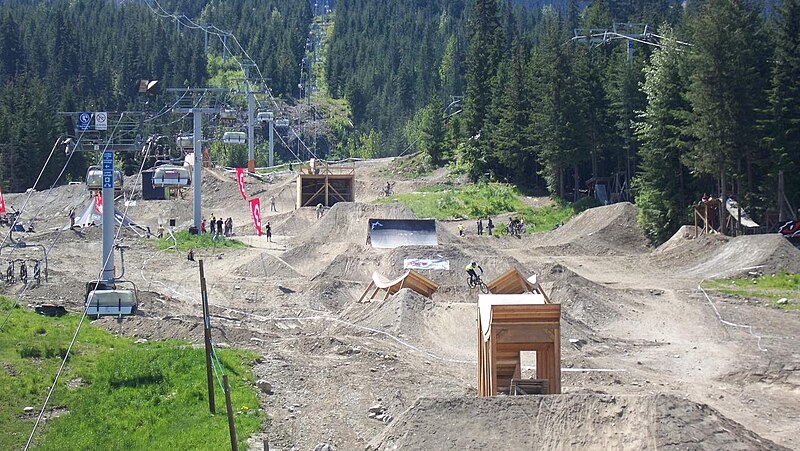 En été, des télésièges surplombent des modules de VTT en terre dans un bike park